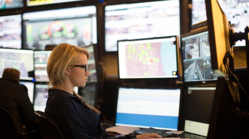 a woman sits at a desk in front of several computer screens