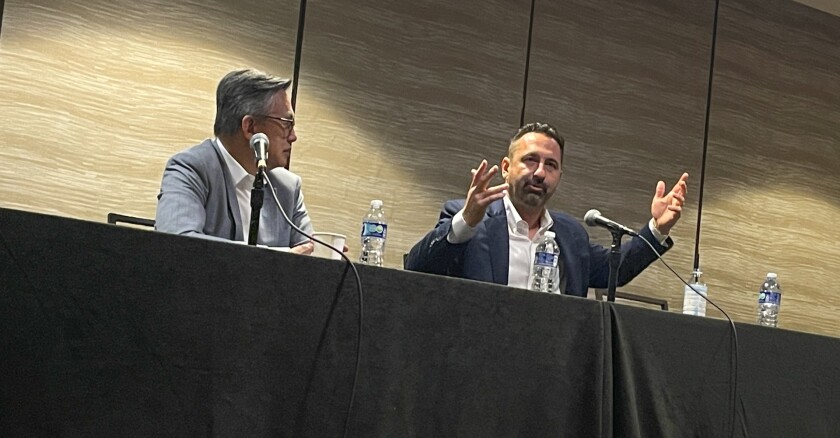 Peter Loo and Ted Ross seated at a table speaking at a conference.