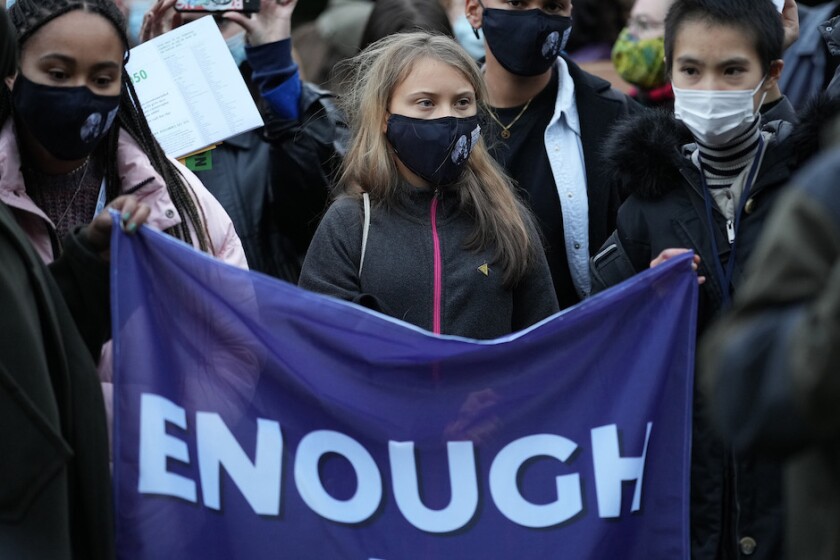 Climate activist Greta Thunberg wearing a facemask and holding a flag that reads "enough."