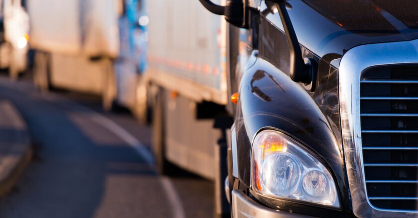 Close-up of a semitruck's headlight. Other semis can be seen in the blurred background.