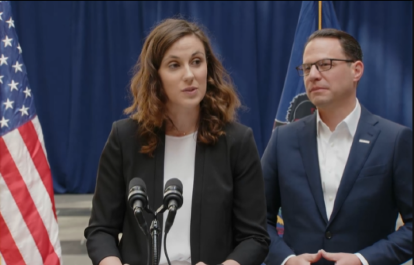 Bryanna Pardoe stands at podium with microphone. American flag hangs on the left. Josh Shapiro stands by her shoulder at the right.
