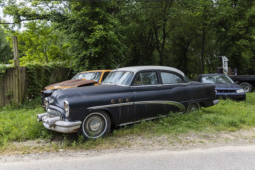 Rusting cars abandoned on the side of a road.