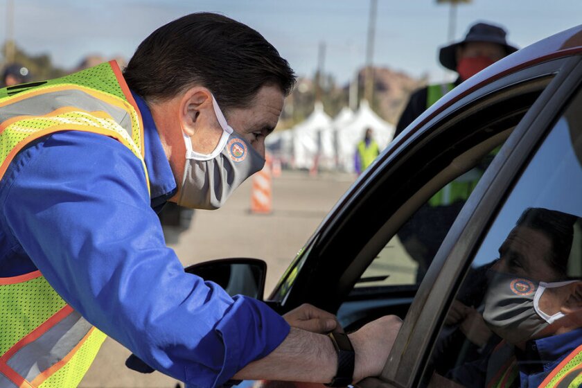 Gov.+Doug+Ducey+weaing+a+mask+talks+to+an+Arizona+resident+sitting+in+a+car.