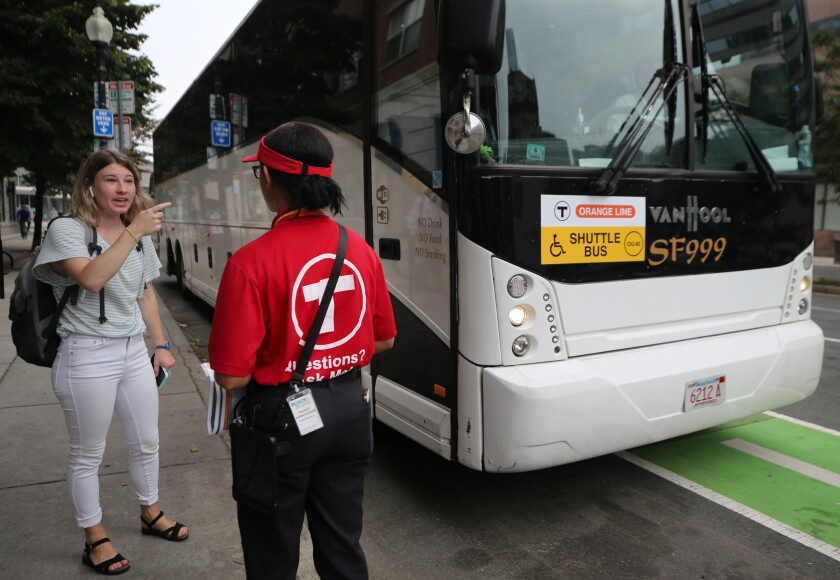 A T Ambassador standing outside a parked bus talking with a passenger.