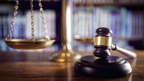 A gavel resting on a pedestal on a wooden table with a set of brass scales in the background.